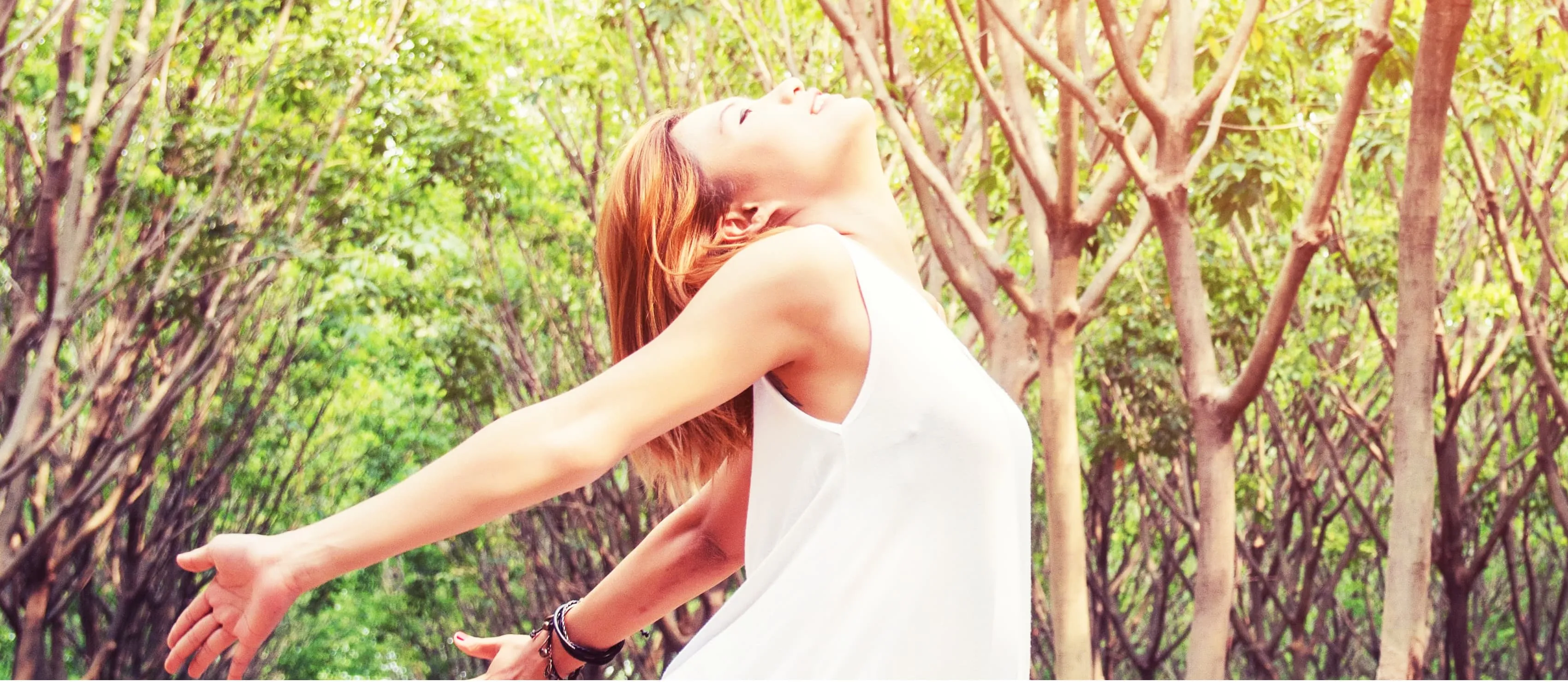 Young beautiful woman raised arms enjoying the fresh in green forest
