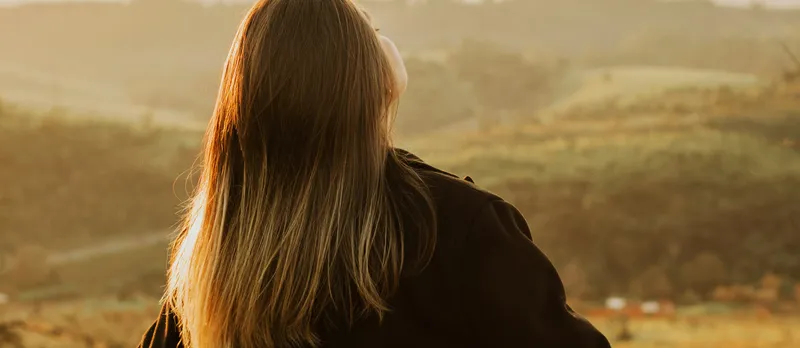 Photo from behind a woman in a field breathing.