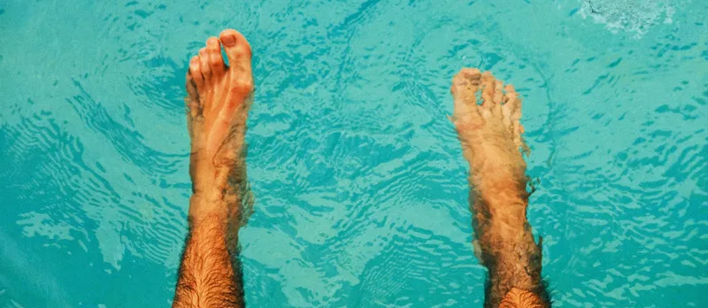Man's feet in cool swimming pool water