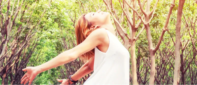 Young beautiful woman raised arms enjoying the fresh in green forest